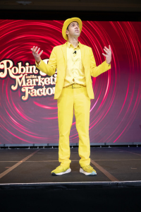 Jesse Cole speaking on stage at Robin Robins' Marketing Boot Camp, wearing his iconic yellow suit during a keynote on standing out in business.